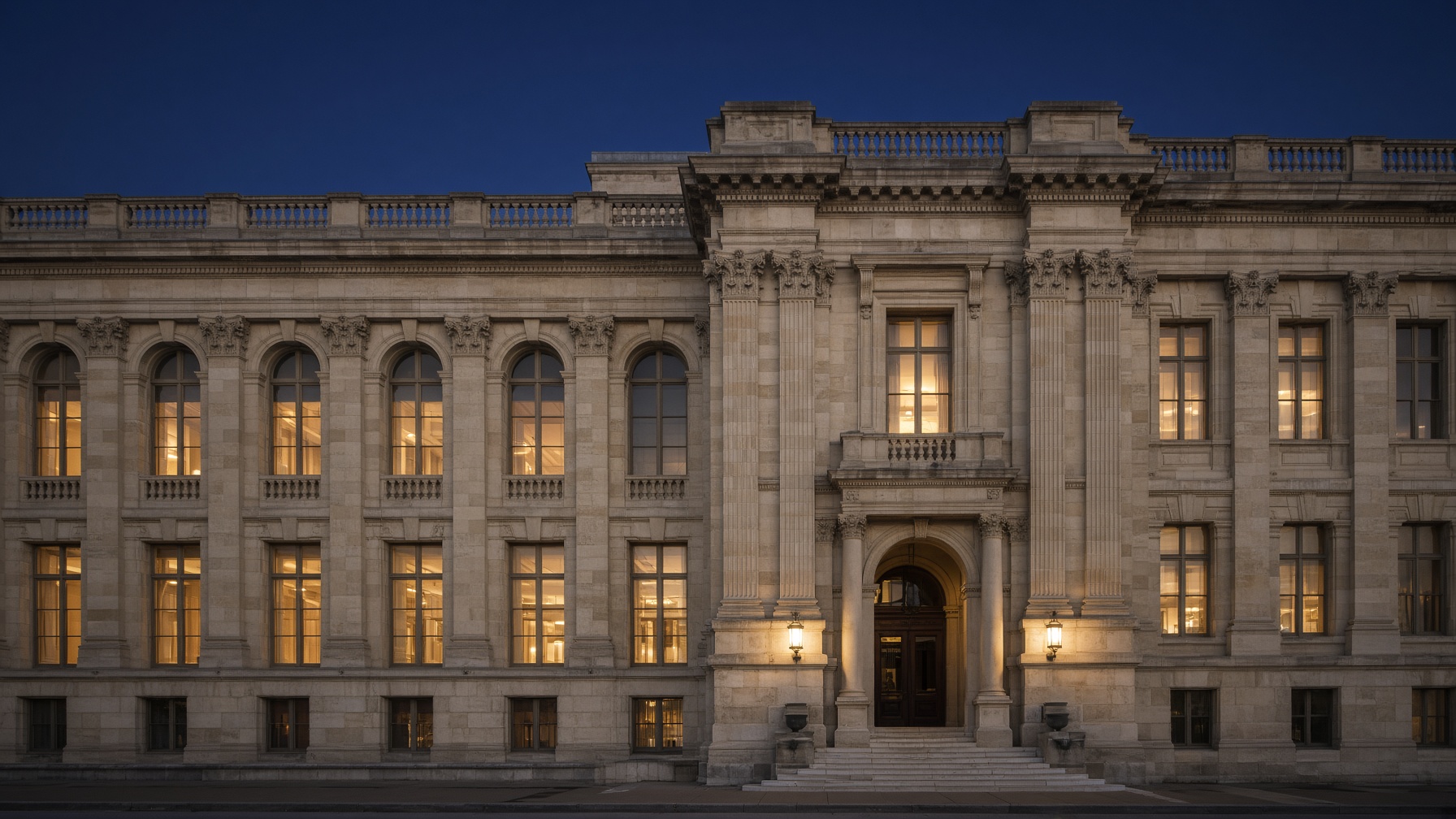 Limestone civic building at twilight, warm windows in a navy sky.